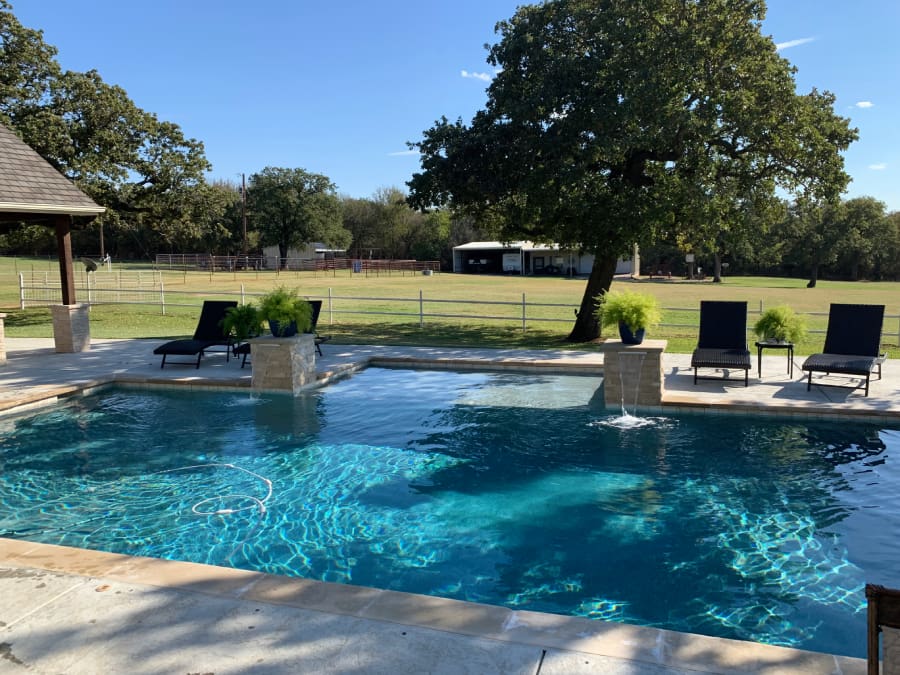 A pool with chairs and trees in the background